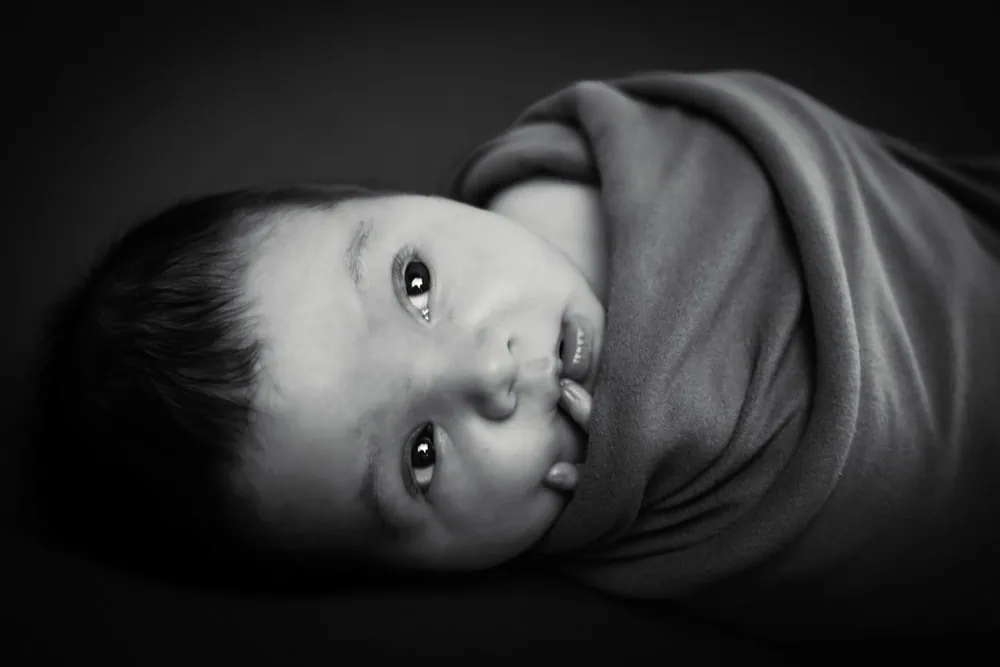 A dramatic black and white portrait of an infant wrapped in fabric.